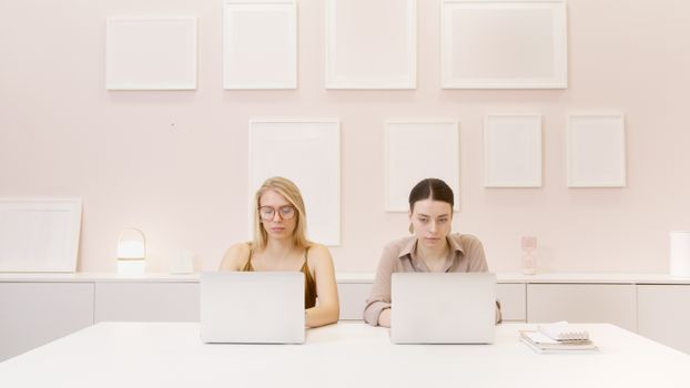 Two professionals working at laptops in a minimalist office setting.
