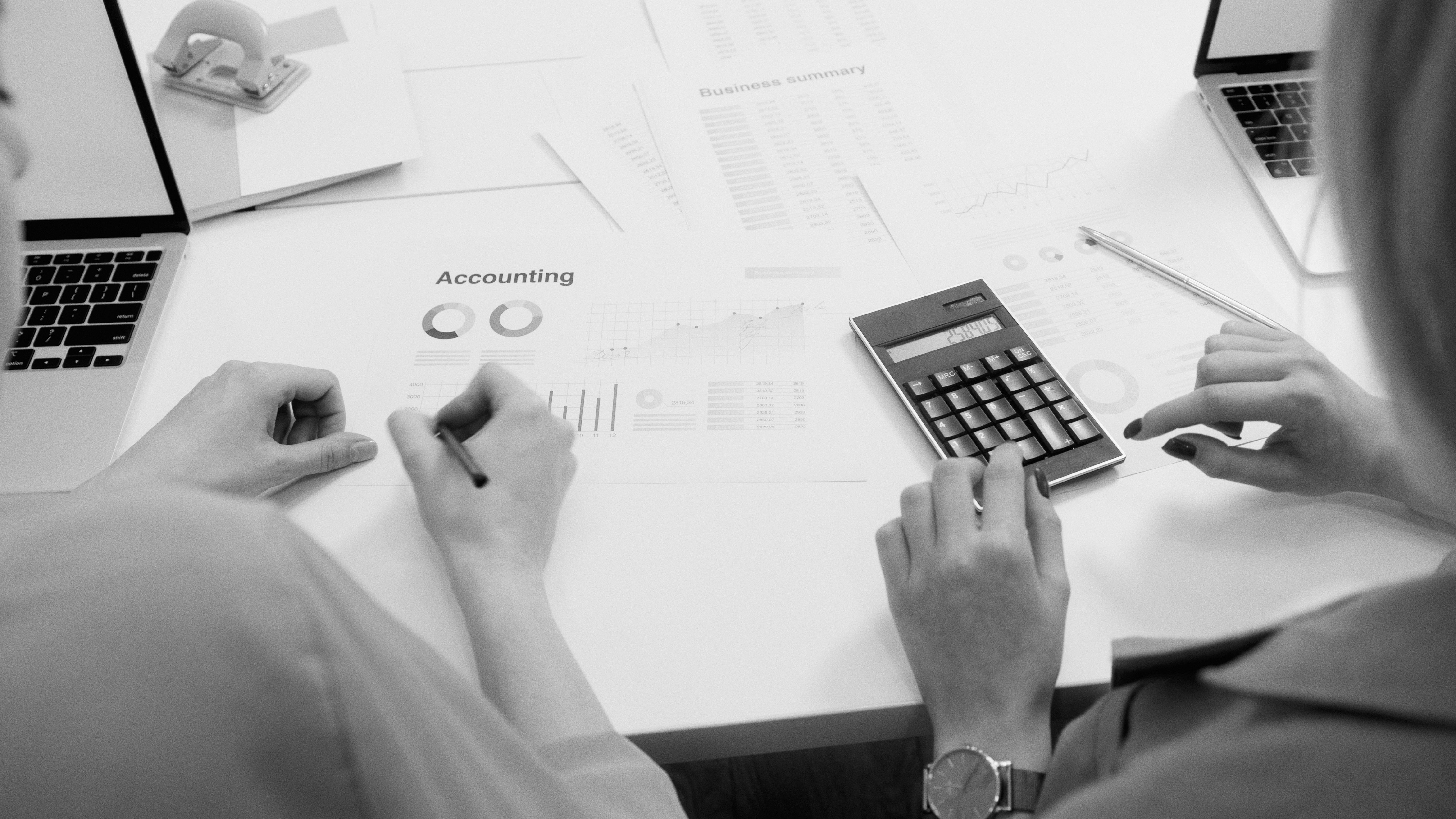 Black and white office scene featuring accounting documents, calculator, and laptops.