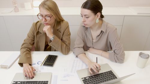 Free Two women working together with laptops and documents in a contemporary office setting. Stock Photo