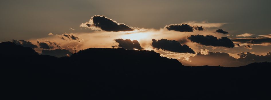 A moody sunset casting dramatic shadows over mountain silhouettes with clouds.