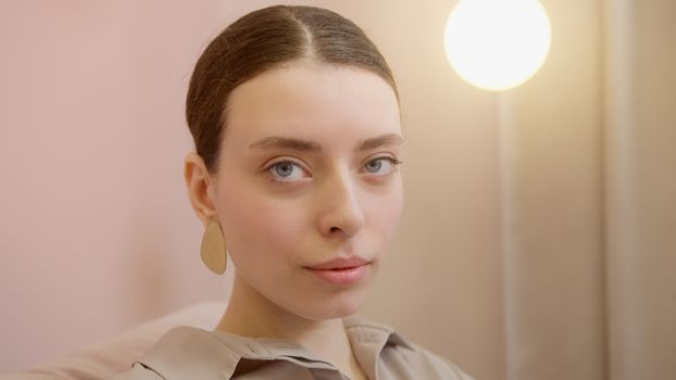 Portrait of a young woman with blue eyes, wearing earrings and a nose piercing, indoors with soft lighting.