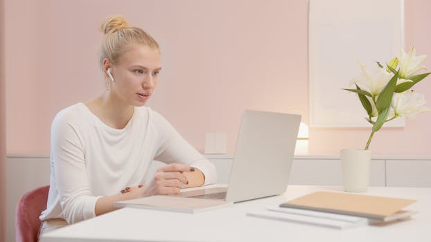 Focused woman in modern office using laptop with AirPods, surrounded by minimalist decor.
