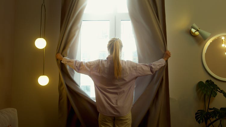 A Woman Opening The Curtains Of A Window 