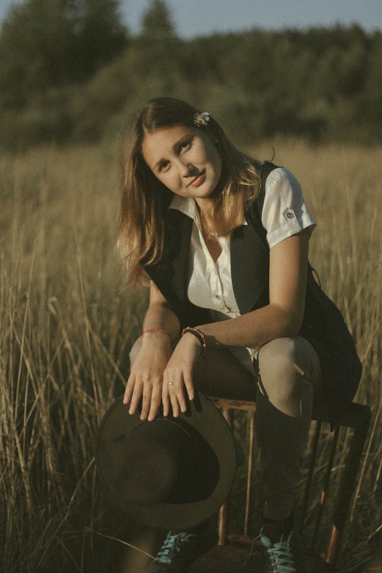 Young Woman Sitting On Back Of Chair In Field