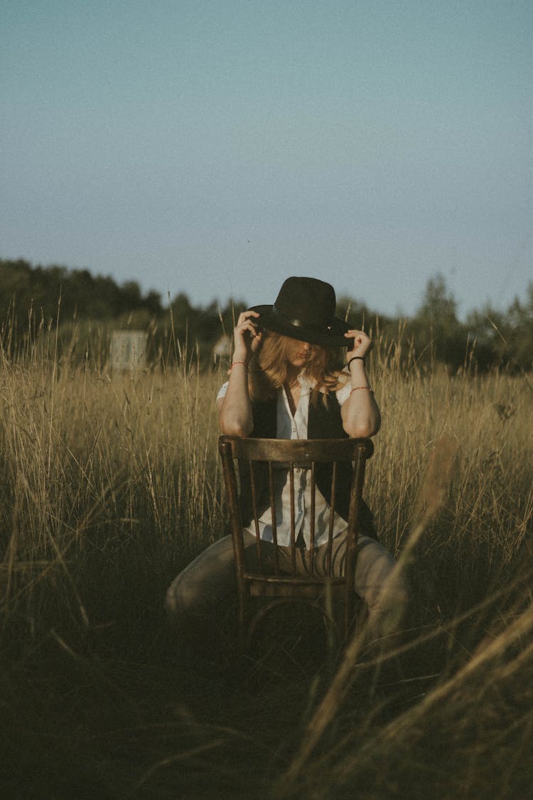 Anonymous Woman With Hat On Head Leaning Elbows On Back Of Chair