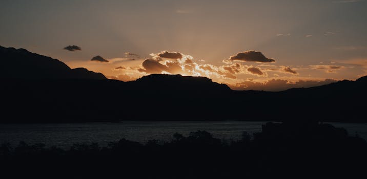 Captivating sunset with silhouetted mountains and calm river beneath golden clouds.