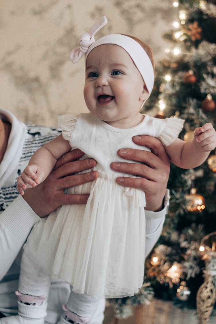 Little Baby In Hands Of Father Near Christmas Tree