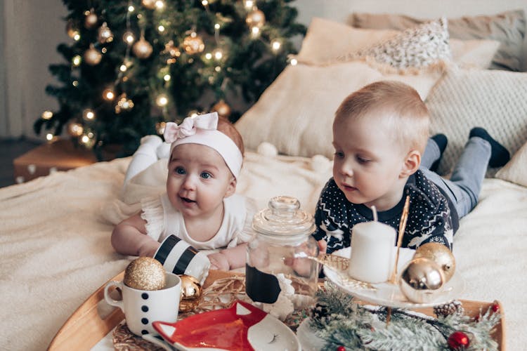 Little Children Lying On Bed Near Christmas Tree