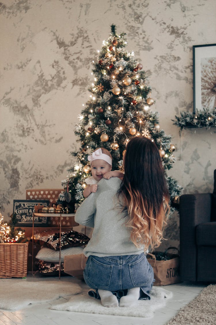 Mother Holding Baby While Sitting Near Christmas Tree