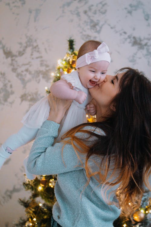 Mother kissing child near Christmas tree at home