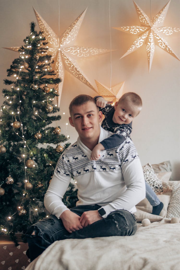 Father With Child On Bed Near Christmas Tree At Home