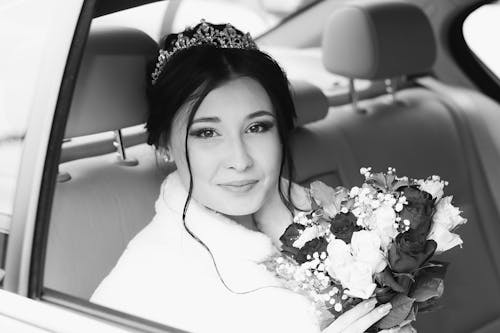 Happy bride sitting with bouquet of flowers in car