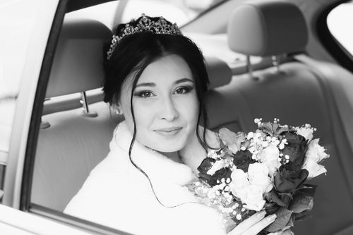 Free Black and white of positive bride with dark hair in stylish clothes sitting with bouquet of flowers in car and looking at camera Stock Photo