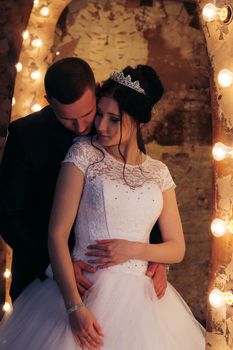 Bride and groom sharing a tender embrace surrounded by glowing lights.
