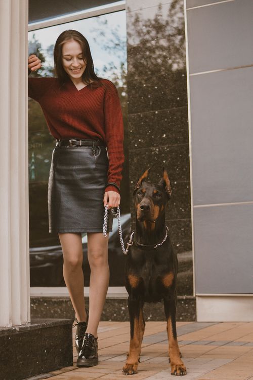 Free Chic woman in urban setting with a Doberman on a leash, exuding confidence. Stock Photo