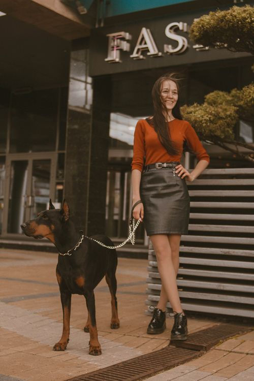 Free Confident woman posing with Doberman on leash outside a fashion store in a city setting. Stock Photo