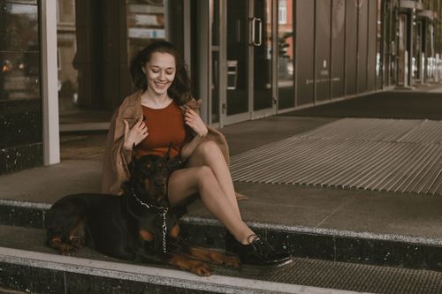 Free Happy woman sitting on steps with a Dobermann dog. Urban outdoor scene. Stock Photo
