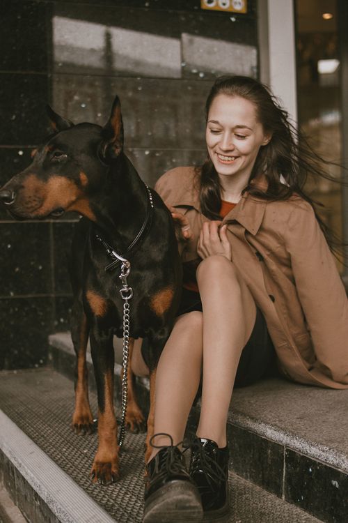 Free Young woman sitting with a Dobermann dog in an urban setting, enjoying a moment together. Stock Photo