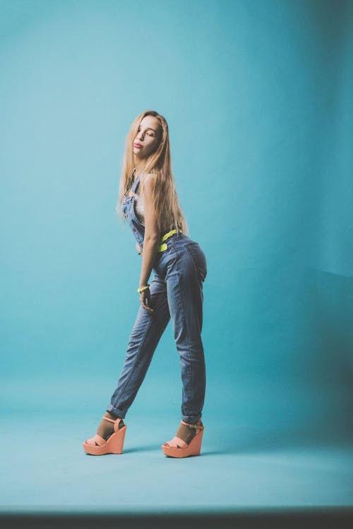 Full body side view of young female in casual outfit and platform shoes with pouting lips standing in studio