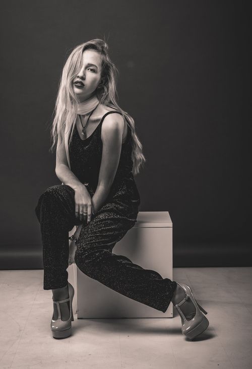 Free Black and white full body of female in jumpsuit and high heels sitting on cube and looking at camera Stock Photo