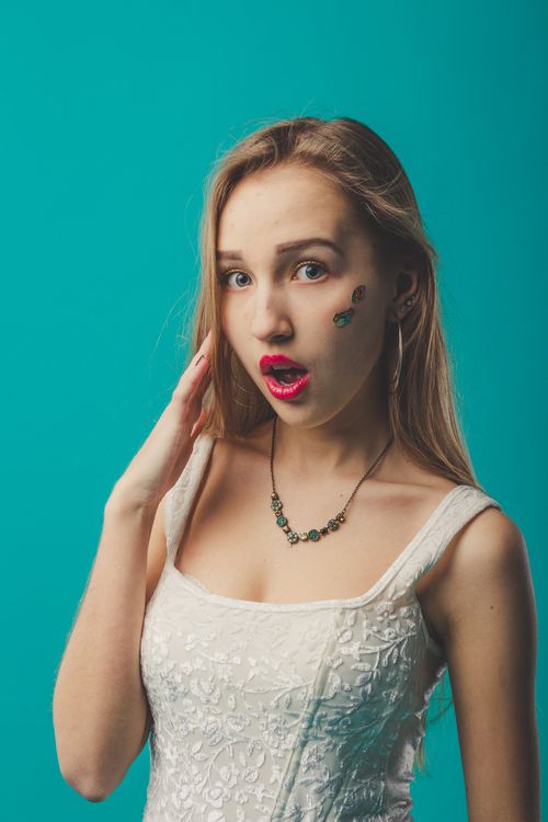 Free Young surprised female with mouth opened touching face against blue background in studio and looking at camera Stock Photo