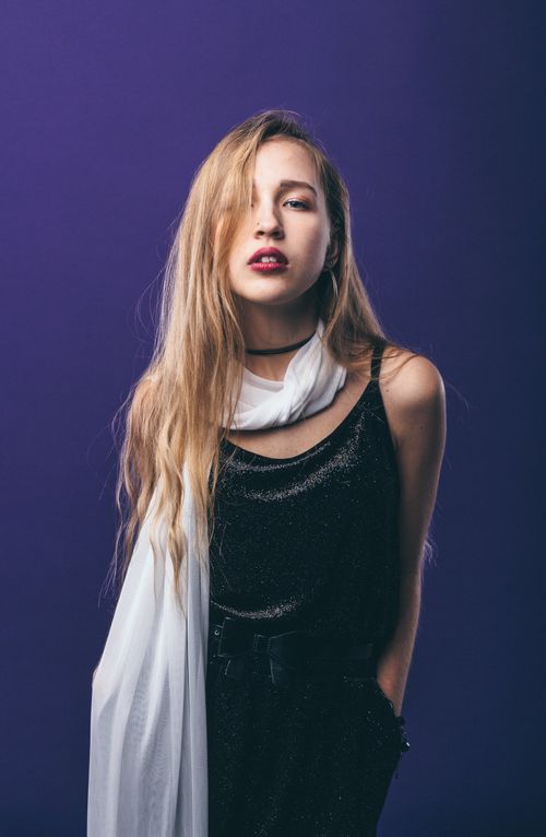 Free Provocative female wearing stylish outfit with long hair standing with hands in pockets against blue background and looking at camera Stock Photo