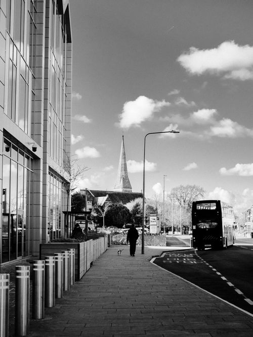 Free Monochrome cityscape featuring a person walking a dog near a bus and modern buildings. Stock Photo