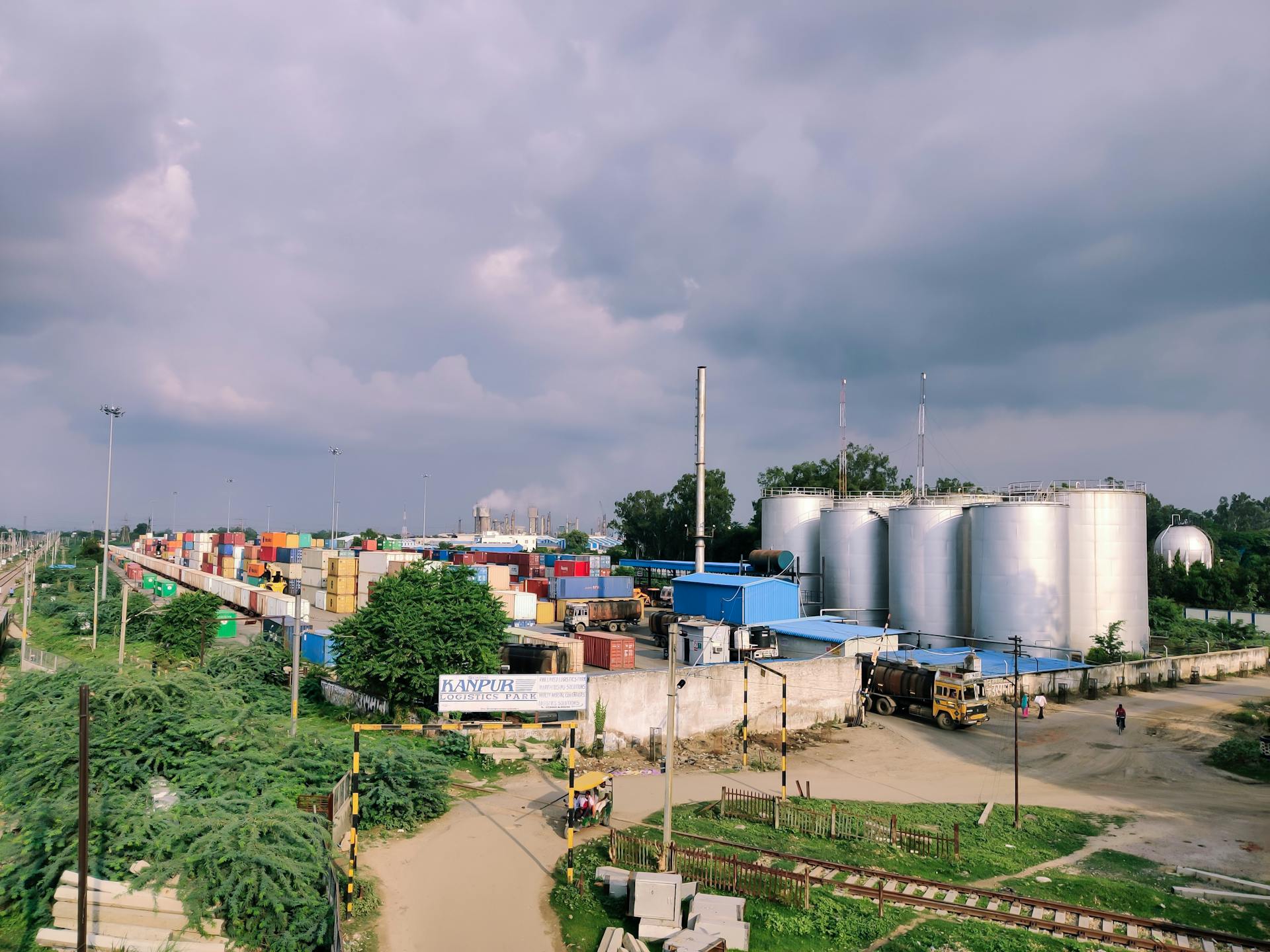 Expansive industrial yard featuring cargo containers and large storage silos under a cloudy sky.