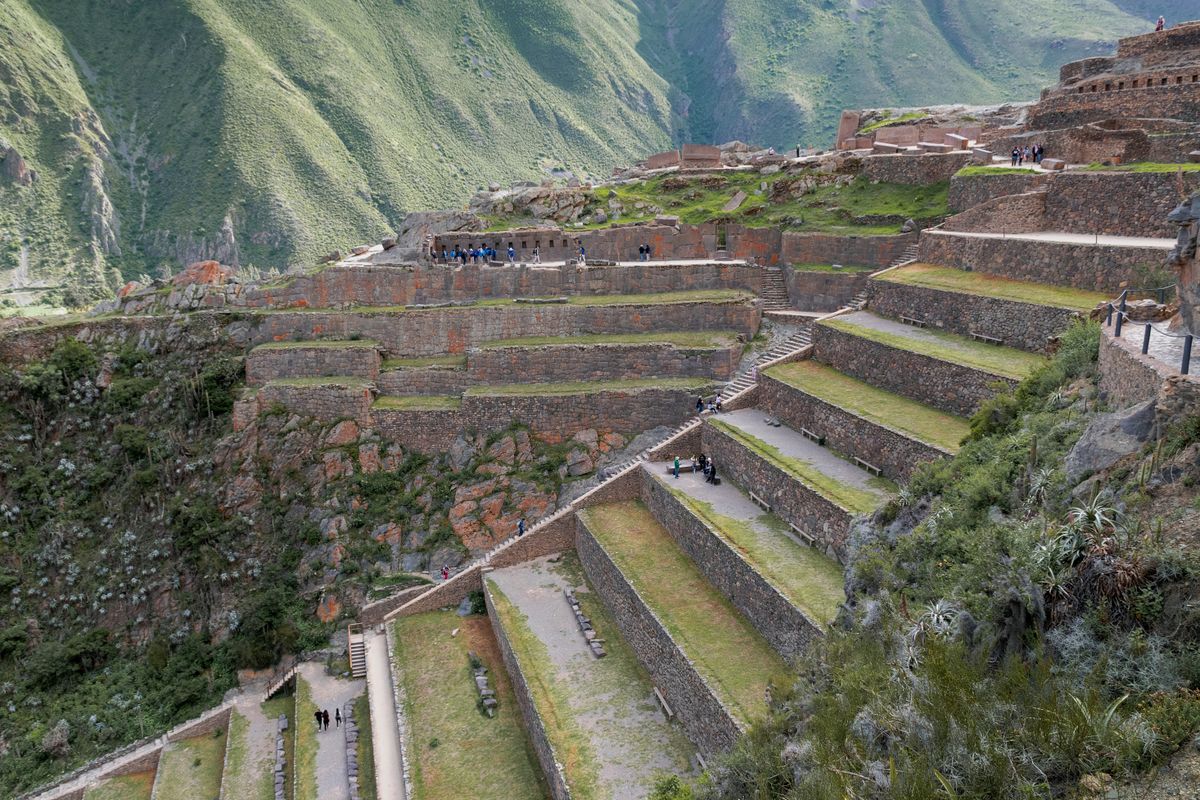 Steep stone-walled terraces climbing a hillside at Ollantaytambo with visitors on the stepped paths for scale