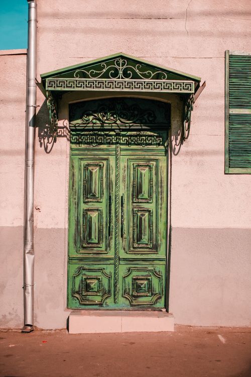 Free Pink stone building facade with decorative elements near pipe and shabby green door in town street in sunny day Stock Photo