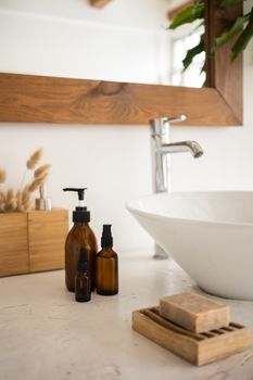 Soap liquid soap and bottles of skincare lotion and oil placed near white sink under mirror in modern bathroom