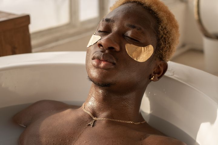 Relaxed African American male with dyed hair lying in bath with milk water and orange slices during spa procedure