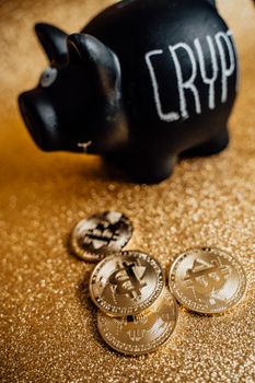 A black piggy bank labeled 'Crypto' with golden bitcoin coins on a sparkling gold surface.
