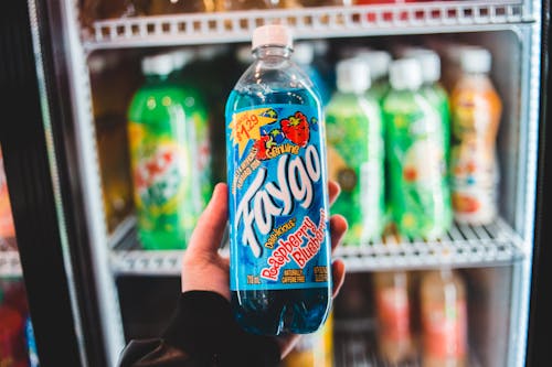 Crop unrecognizable shopper showing bottle of carbonated beverage with raspberry and blueberry flavor against fridge in shop