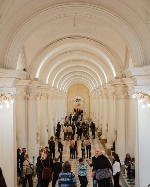Free Crowded majestic palace hallway with tiled floor arched ceilings and white grand columns Stock Photo
