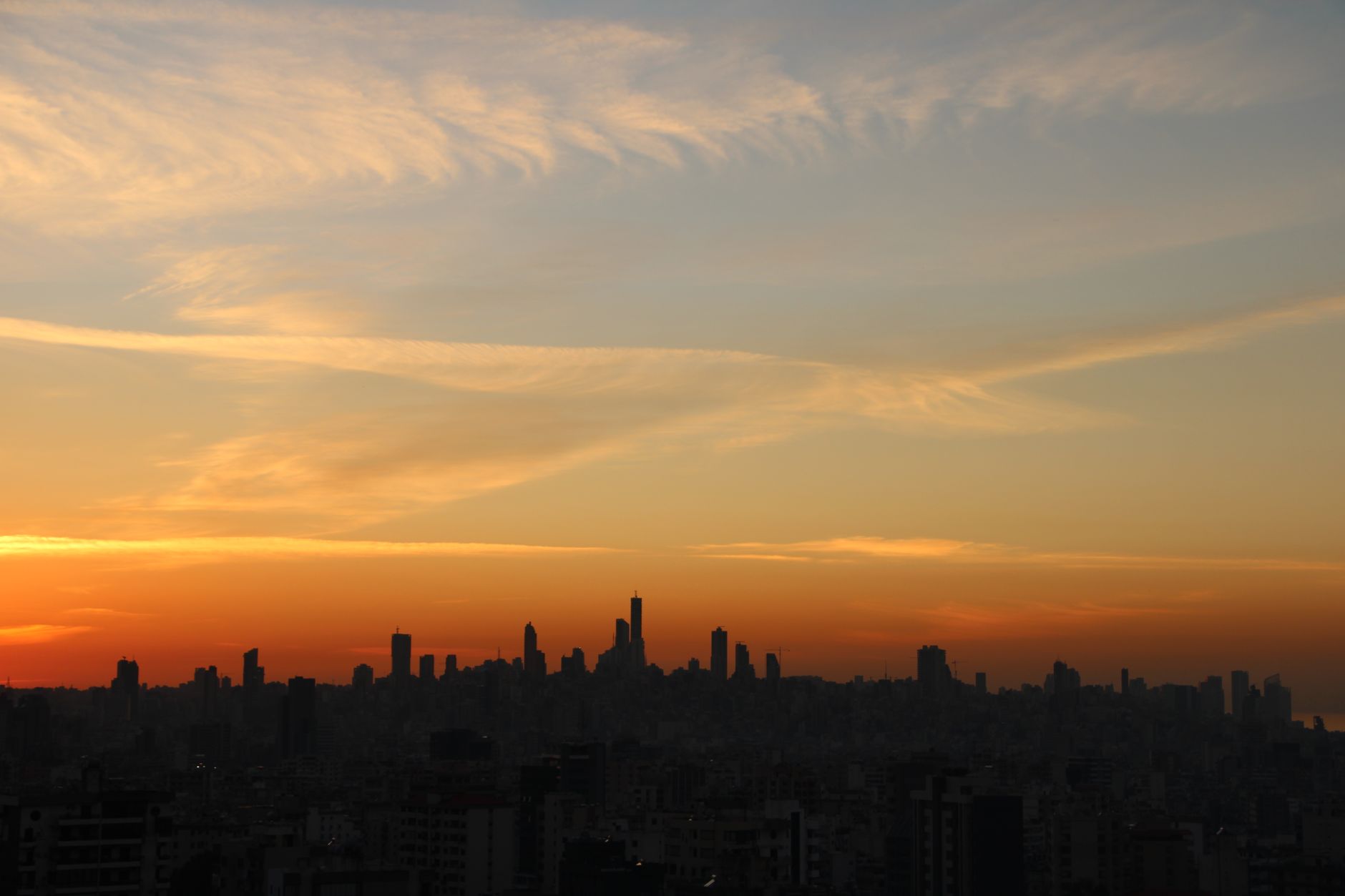 Silhouette of city skyline under a vibrant sunset sky with colorful clouds.