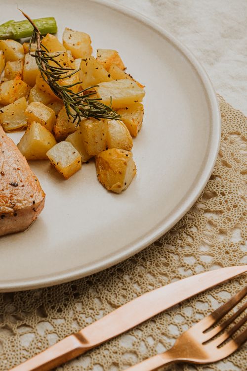 Free A close-up of delicious roasted potatoes and meat garnished with rosemary on a beautifully set table. Stock Photo
