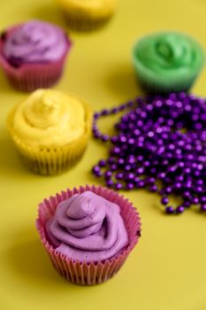 Vibrant Mardi Gras cupcakes topped with colorful icing, accompanied by festive beads on a yellow background.