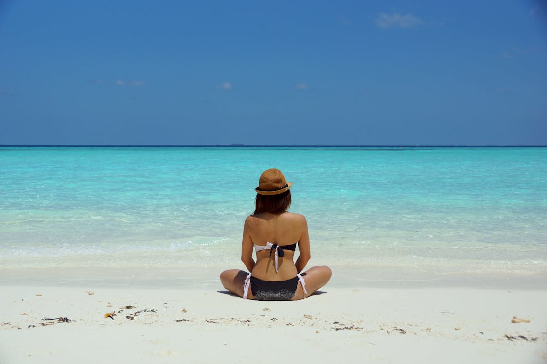 免費 女人穿著黑色和白色的胸罩，坐在白色的沙灘上 圖庫相片