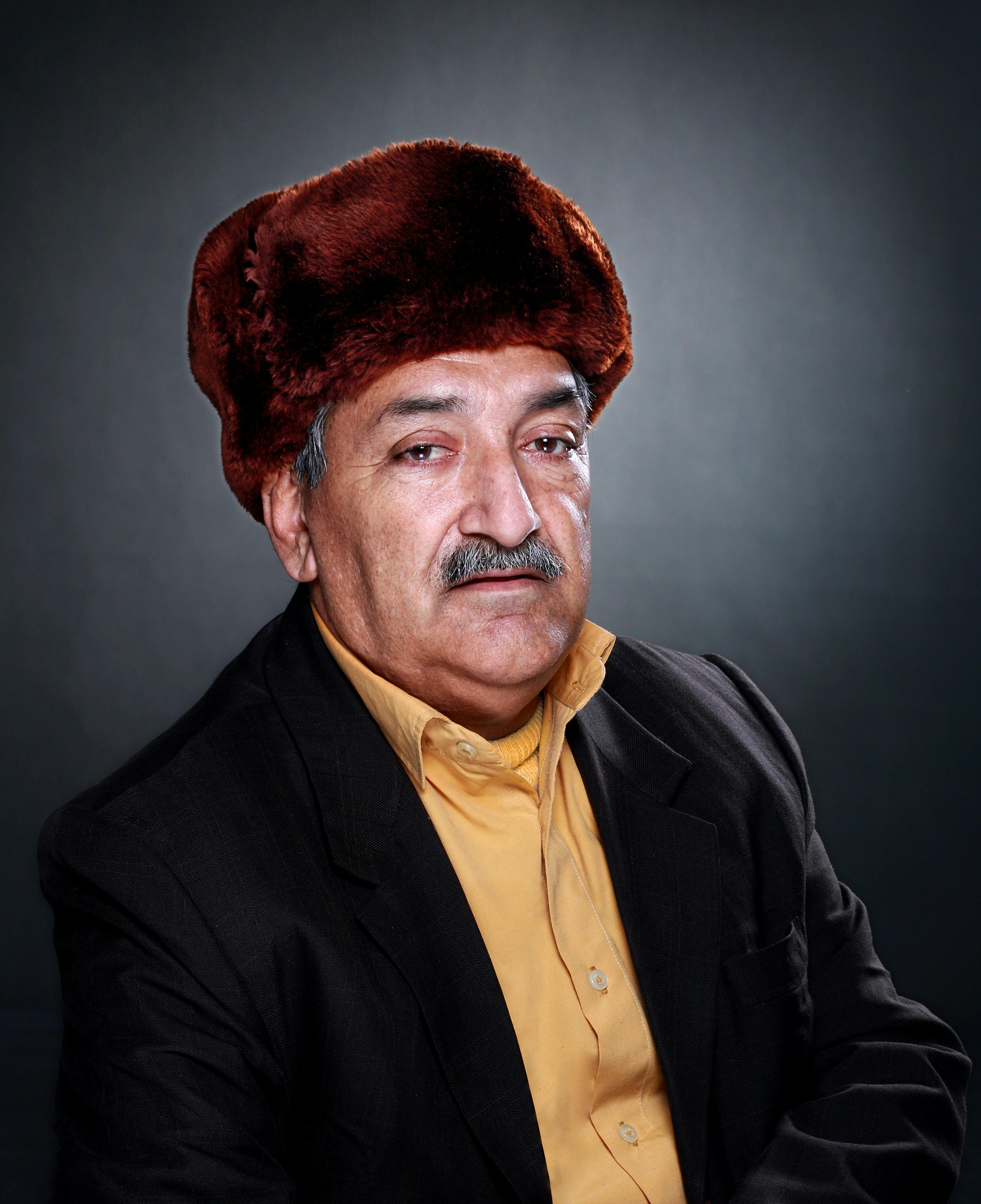 Studio portrait of a senior man in a brown hat and suit with a neutral background.
