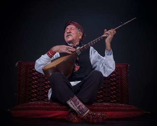 Elderly Man Playing a Guitar and Singing in Traditional Clothing 