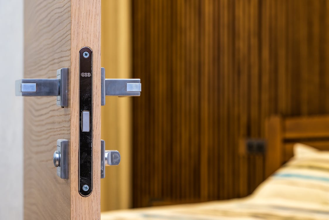 Free Opened doorway with lock and simple metal handle in light room with wooden bed Stock Photo