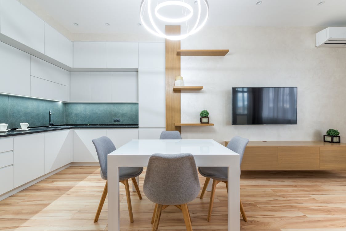 Free Modern flat interior with table with chairs next to shelves and TV on wall near open kitchen with cupboards Stock Photo