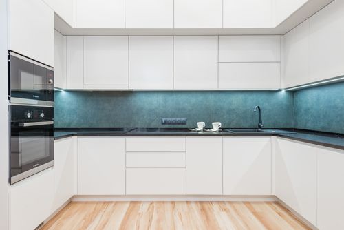 Free Interior of white modern kitchen with minimalist design of white cabinets blue backsplash and black built in appliances Stock Photo