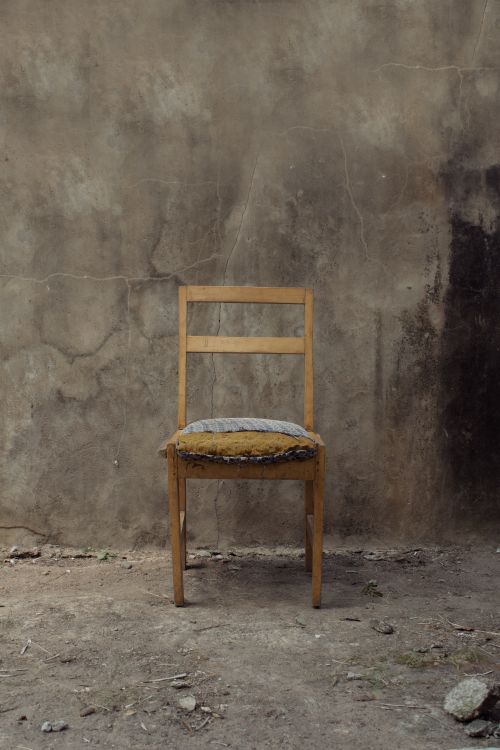 Free Old wooden chair positioned in front of a weathered wall, capturing rustic charm. Stock Photo