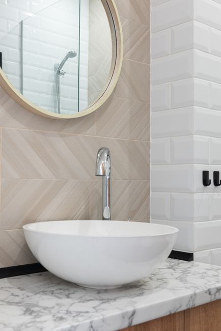 Interior of light modern restroom with sink and faucet on cabinet under mirror on tile wall