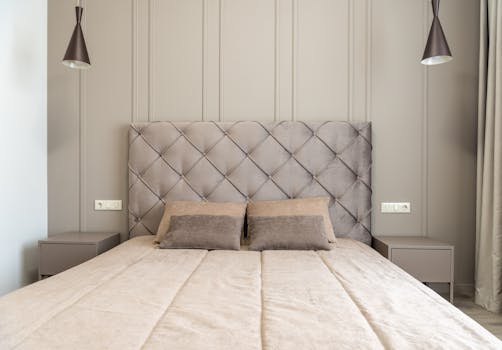 A minimalist modern bedroom featuring a stylish quilted headboard and soft lighting.