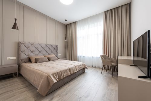 Free Interior of modern bright hotel room with bed with pillows and blanket in front of TV on table next to chair and windows with curtains Stock Photo