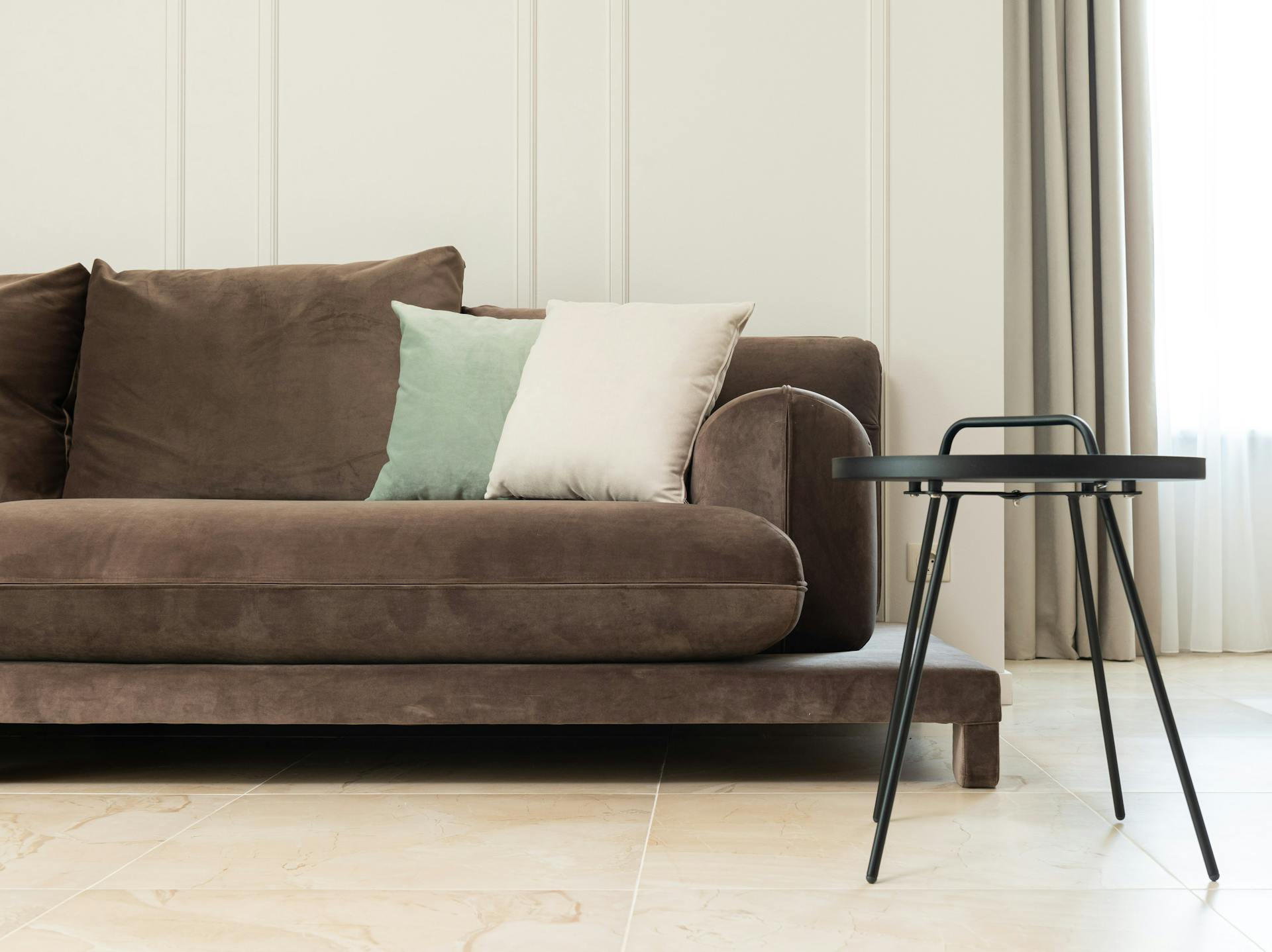 Interior of bright modern flat with couch with pillows near round table and curtains on windows