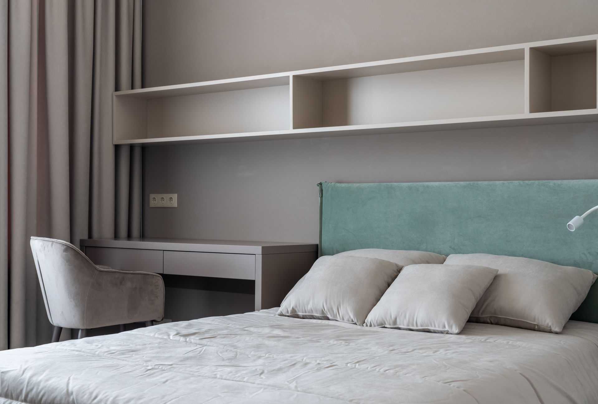 Interior of modern light flat with bed with pillows under shelves near table with chair next to curtains